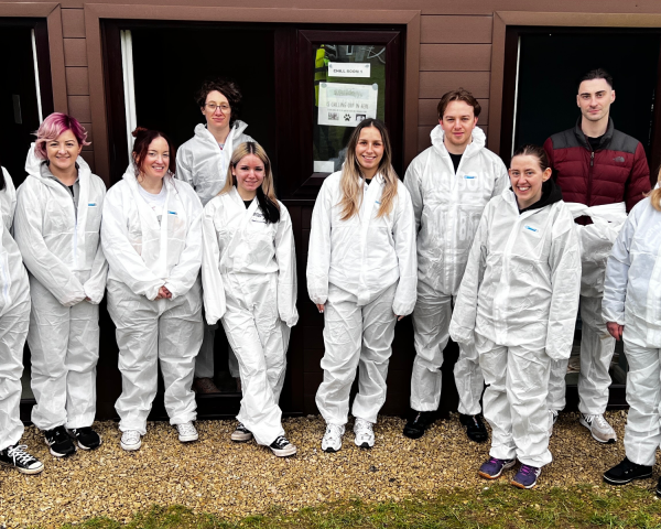 10 individuals wearing white all-in-ones, facing front towards the camera smiling